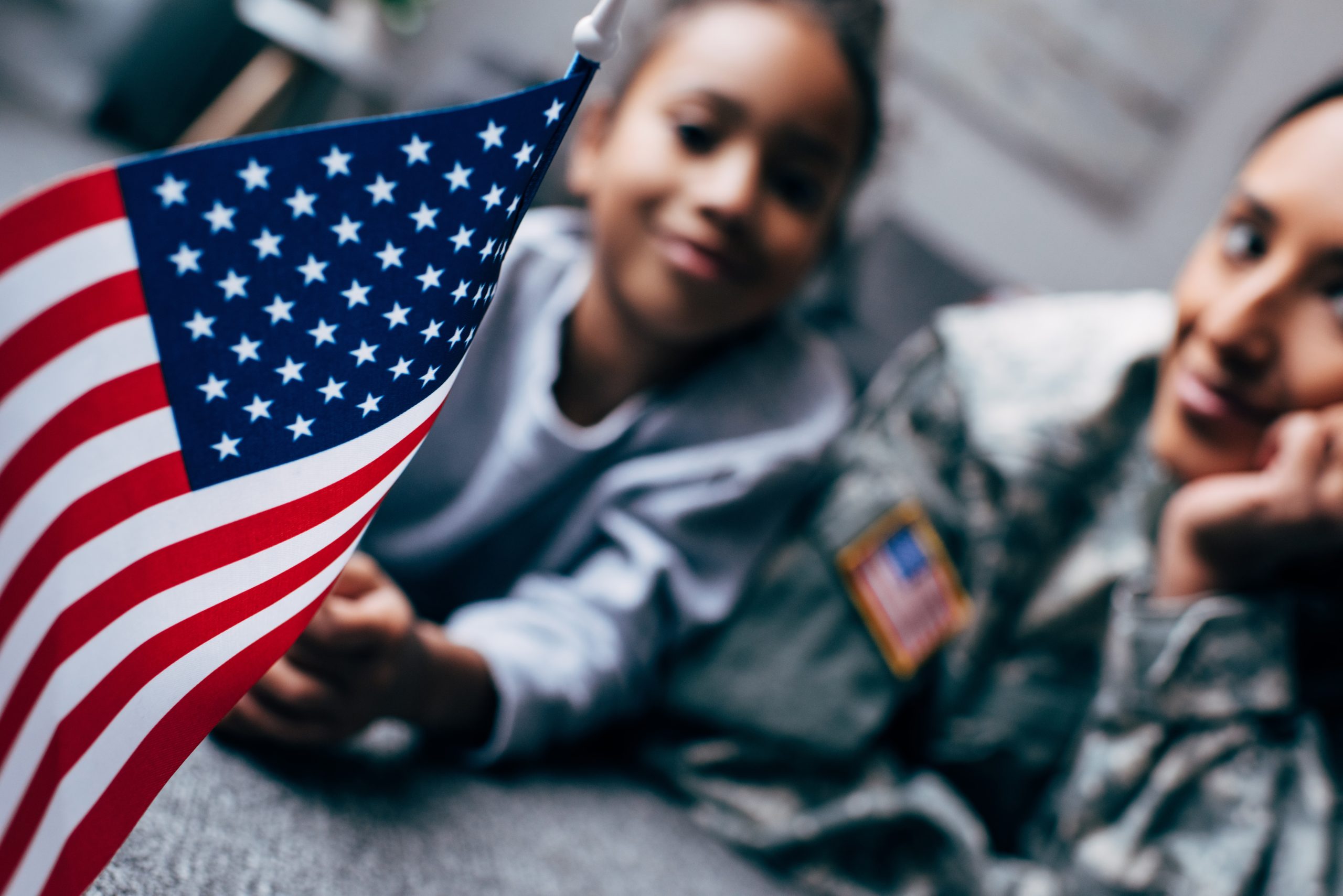 african american daughter and mother in military uniform with american flag at home