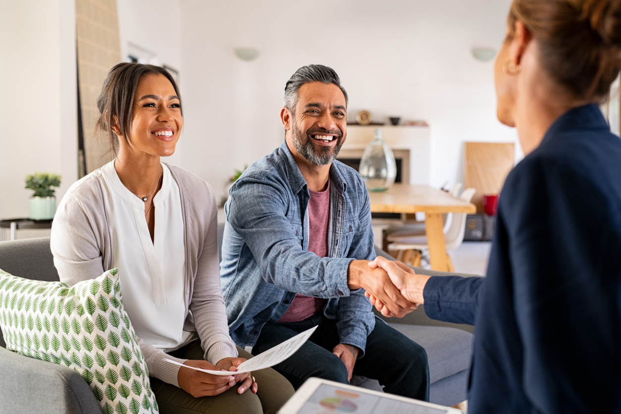 Happy smiling real estate investor couple greeting broker with handshake at home.