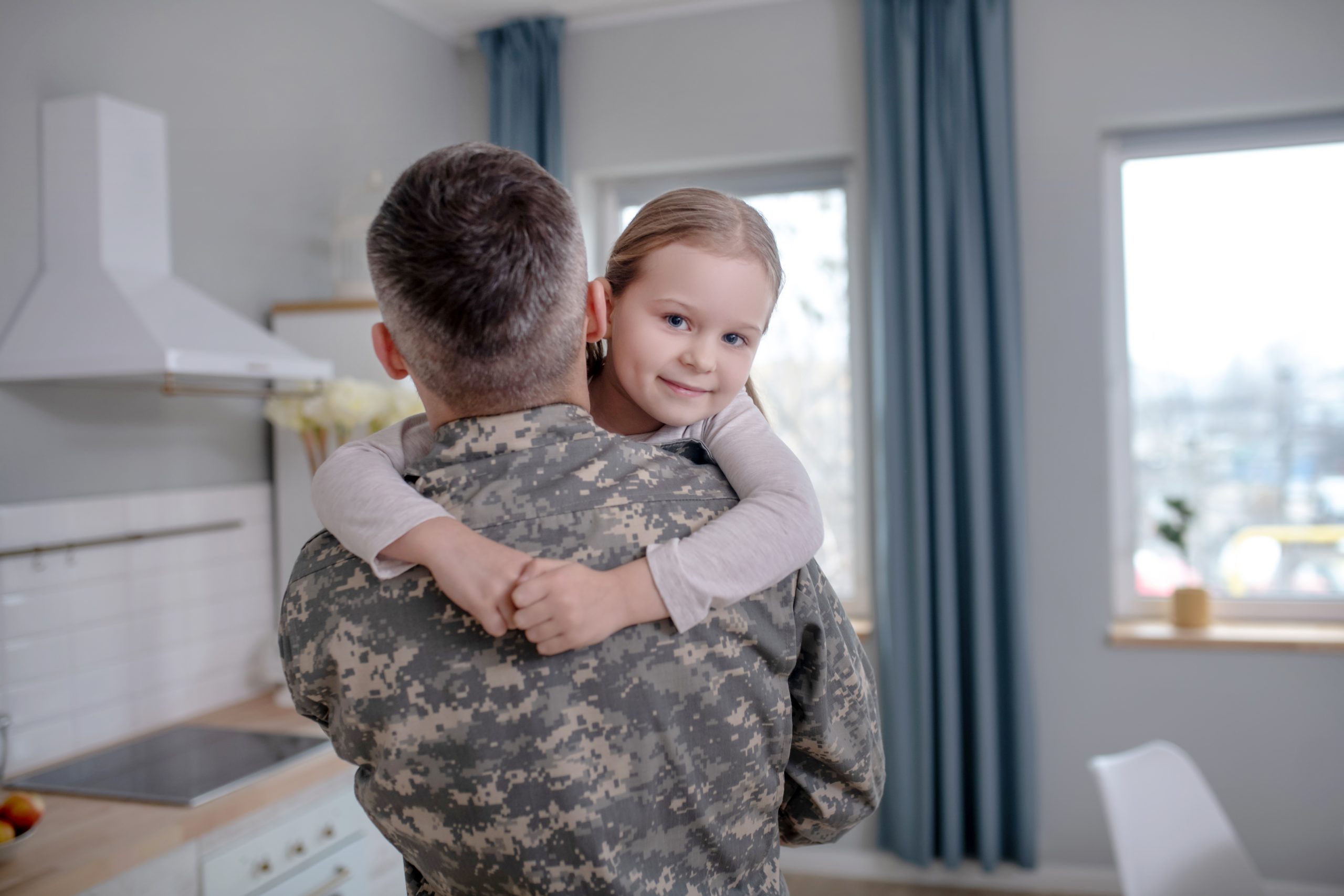 Little happy daughter in the arms of a military officer.
